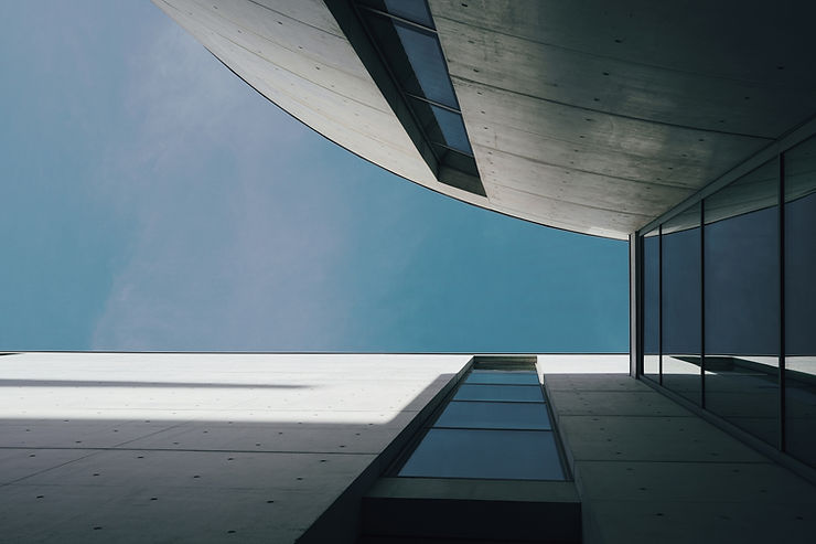 Abstract view of modern architecture with geometric lines, concrete, and reflective glass windows against a clear blue sky.